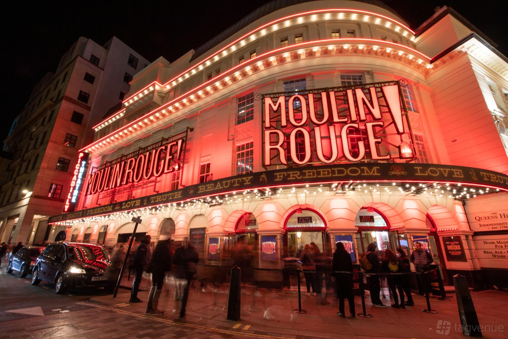 A theatre exterior with illuminated Moulin Rouge signage and marquee lights at ATG VIP: Moulin Rouge - Piccadilly Theatre.