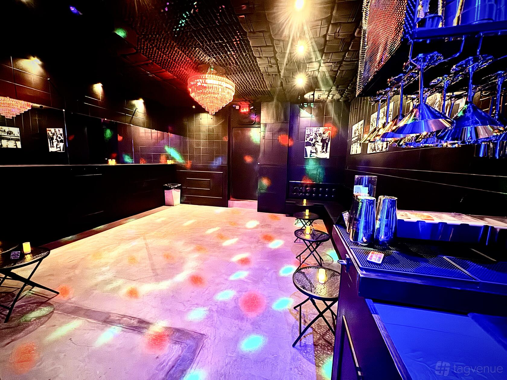A function room with black walls, a chandelier, bar seating, and colorful disco lights at B Lounge NYC.