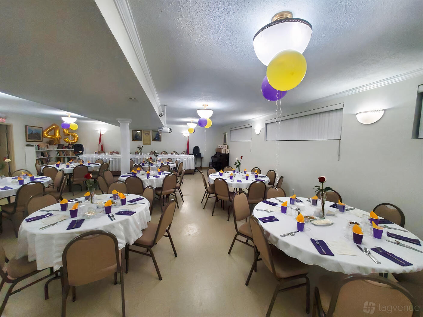 A church hall with round tables covered in white linens, purple napkins, and yellow balloons at St. Mary Armenian Church.