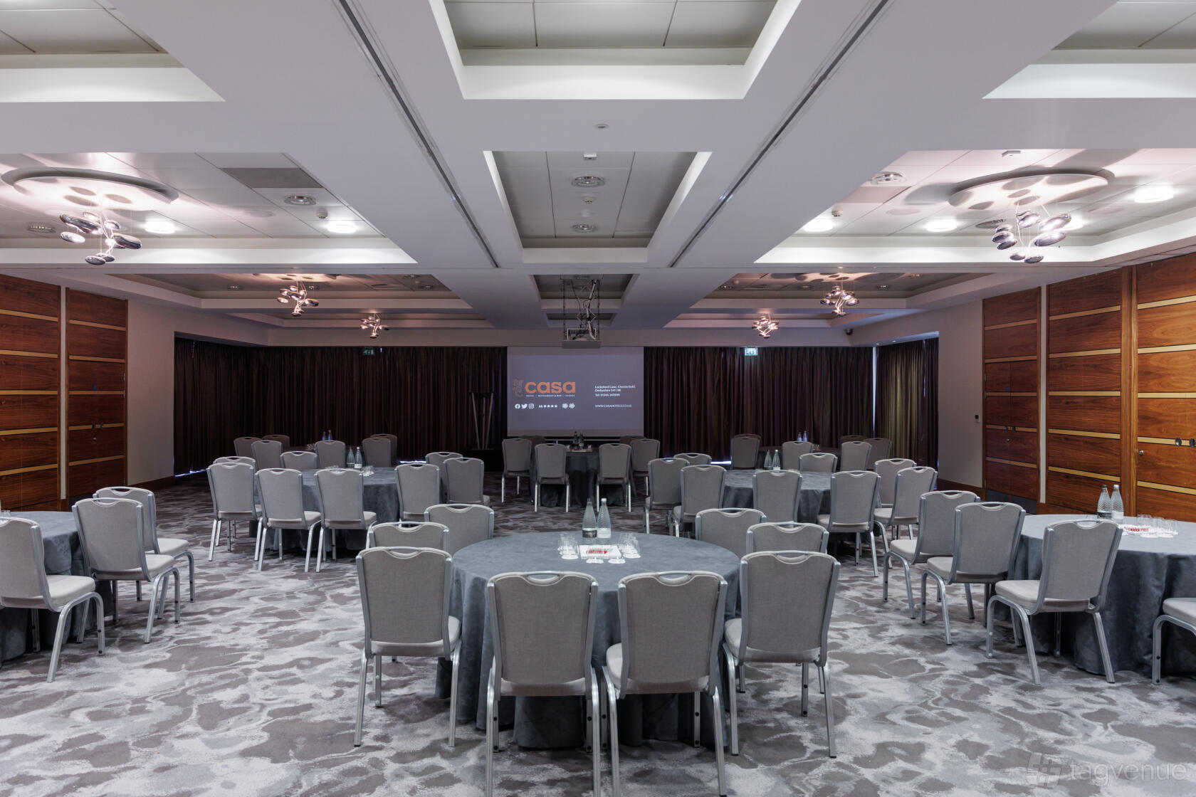 An event space with round tables, gray chairs, patterned carpet, and wood-paneled walls at Casa Hotel.