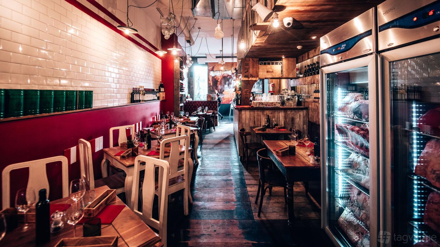 A hotel dining room with wooden floors, red accents, exposed bulbs, and a meat fridge at Macellaio RC Clerkenwell.