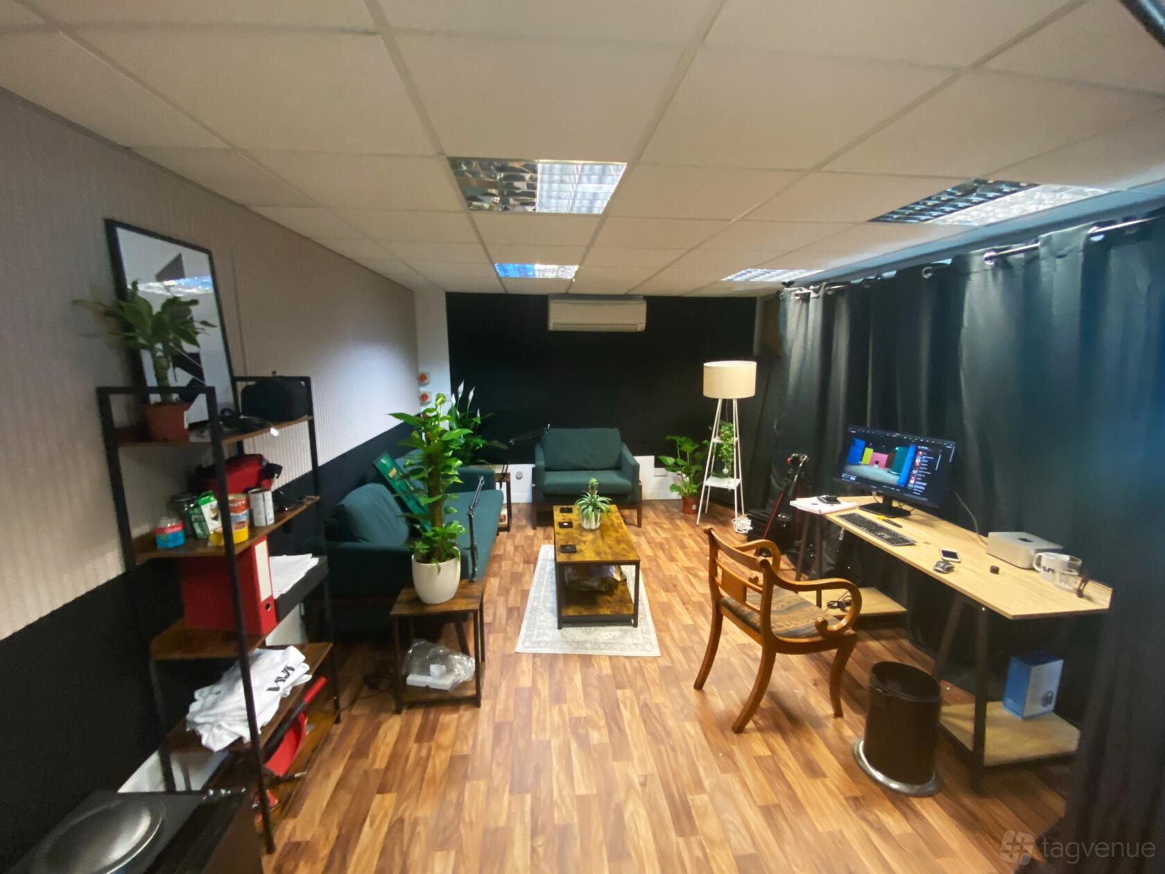 A podcast studio with seating area, desk setup with monitor, wood flooring, and potted plants at Don Doro Studios.