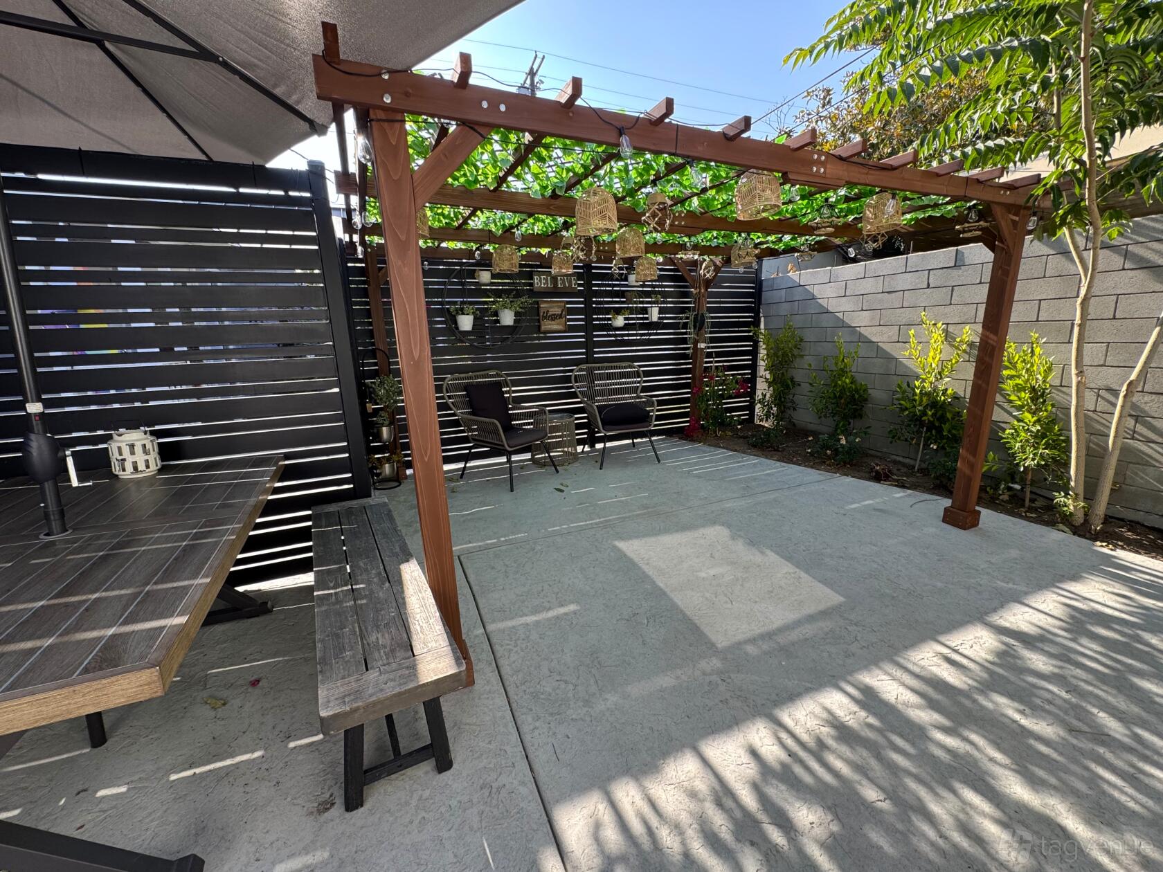 An outdoor venue with a wooden pergola, hanging baskets, and patio seating at Chateau de Luce.