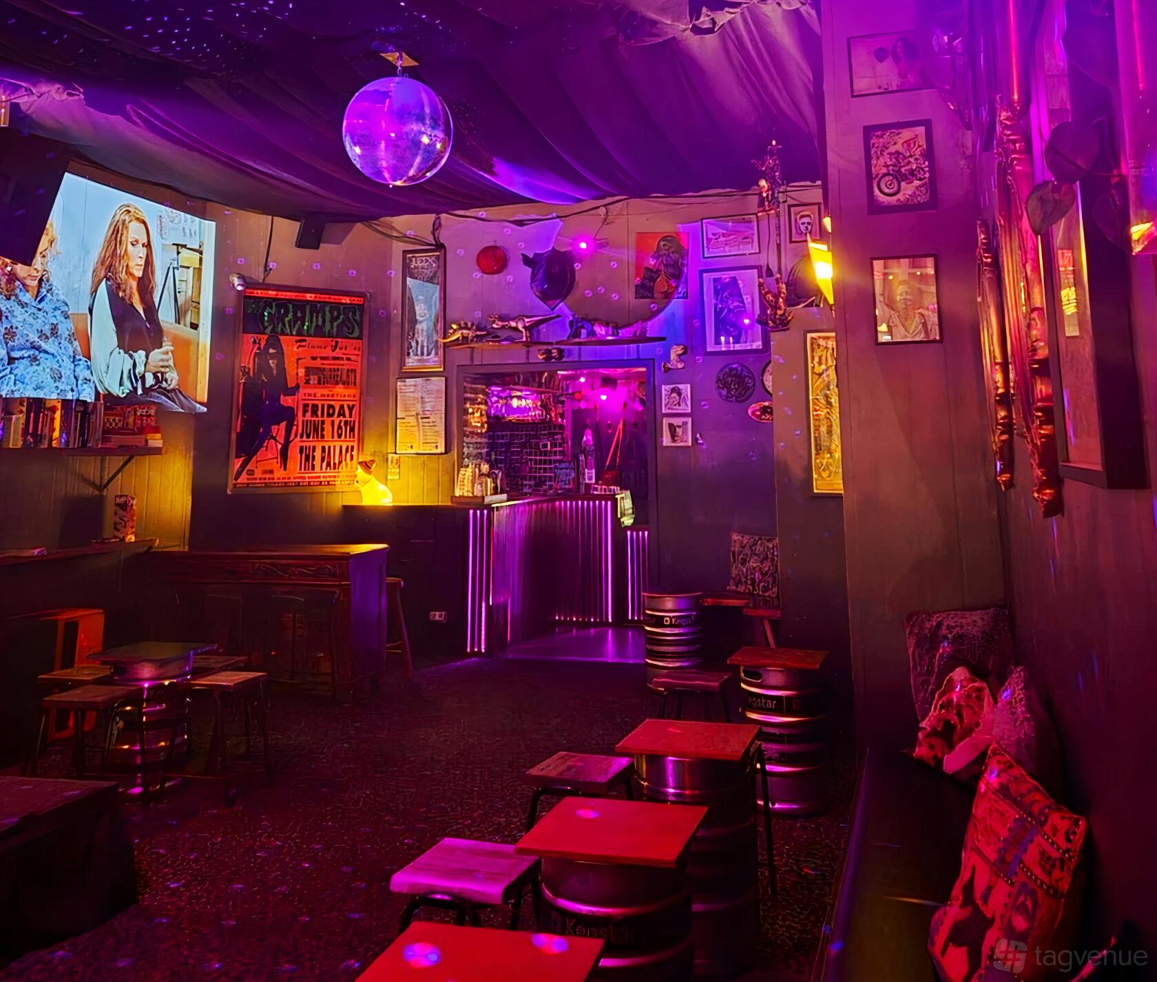 A bar with neon lighting, eclectic wall art, a disco ball, and small wooden tables at Creatures of Habit Bar & Bandroom.
