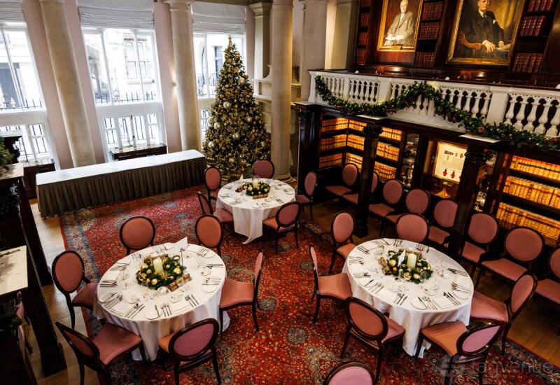 A grand hall with round tables dressed in white linens, festive decorations, and tall windows at One Moorgate Place.