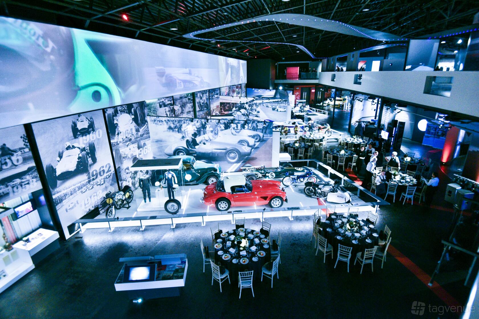 A museum event space with vintage race cars on display and round tables set for dining at Silverstone Museum.
