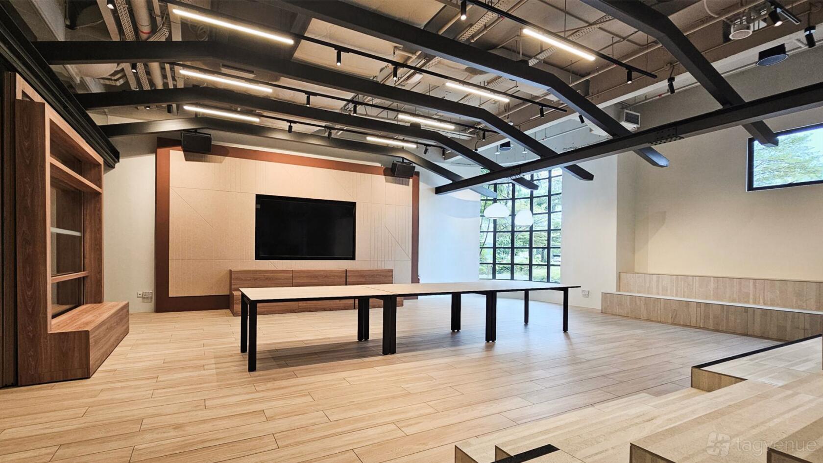 An event venue with exposed ceiling beams, a large screen, and light wood flooring at Pico Event Hall.