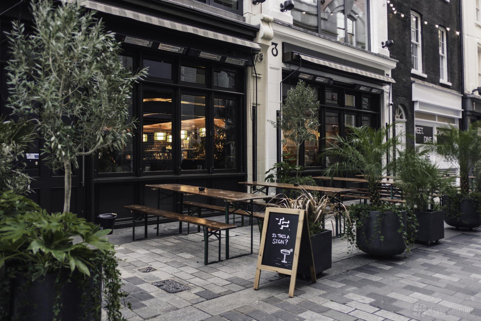 A pub with wooden benches, potted plants, and a chalkboard sign outside the entrance at Two Floors.