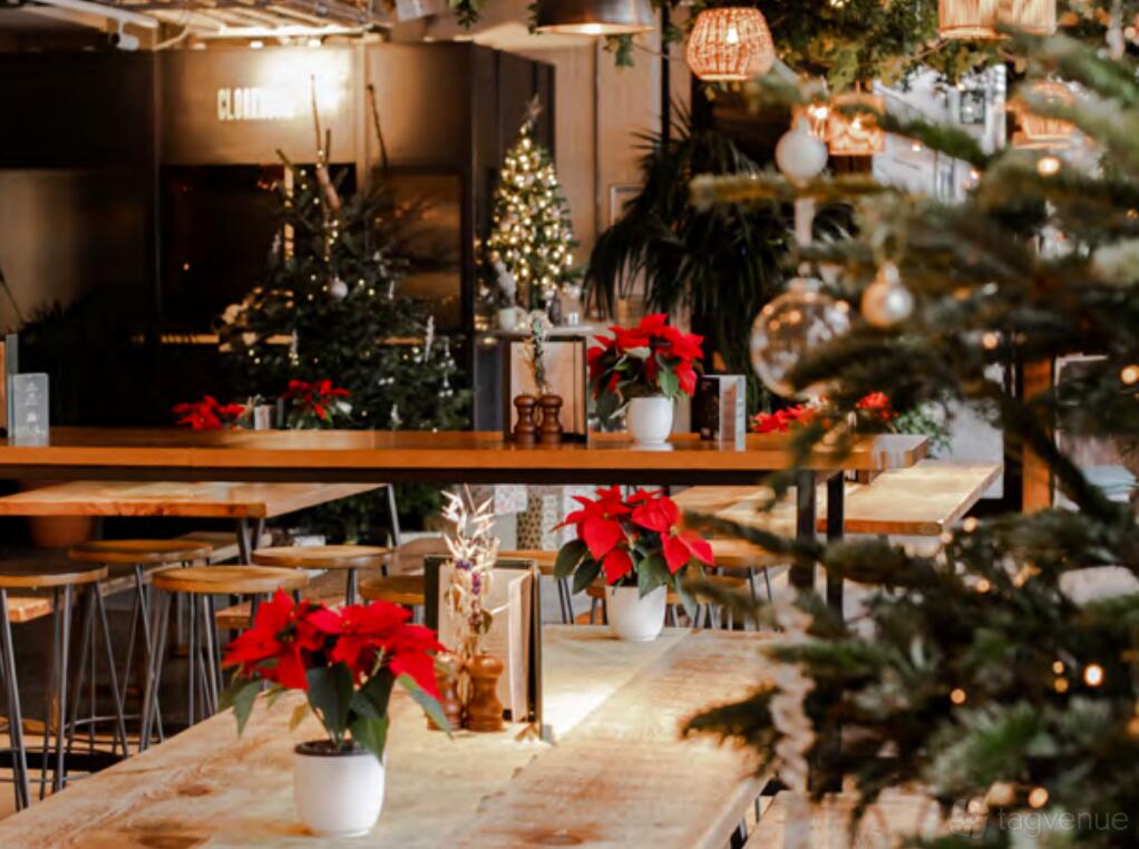A bar with tall wooden tables, festive holiday decorations, and potted poinsettias at Pergola on The Wharf.