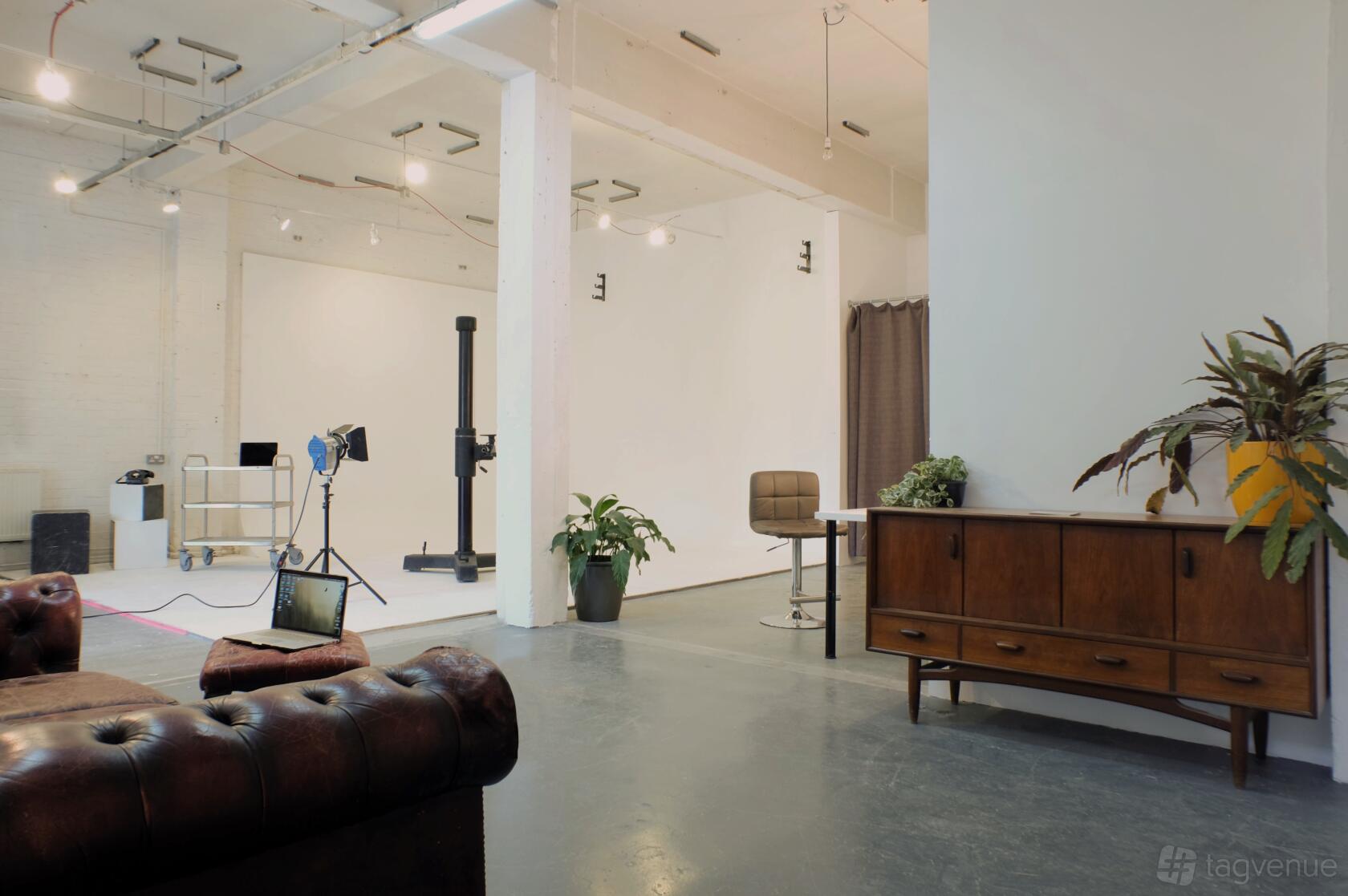 A photo studio with high ceilings, white walls, industrial lighting, and vintage furniture at Mowlem Street Studios.