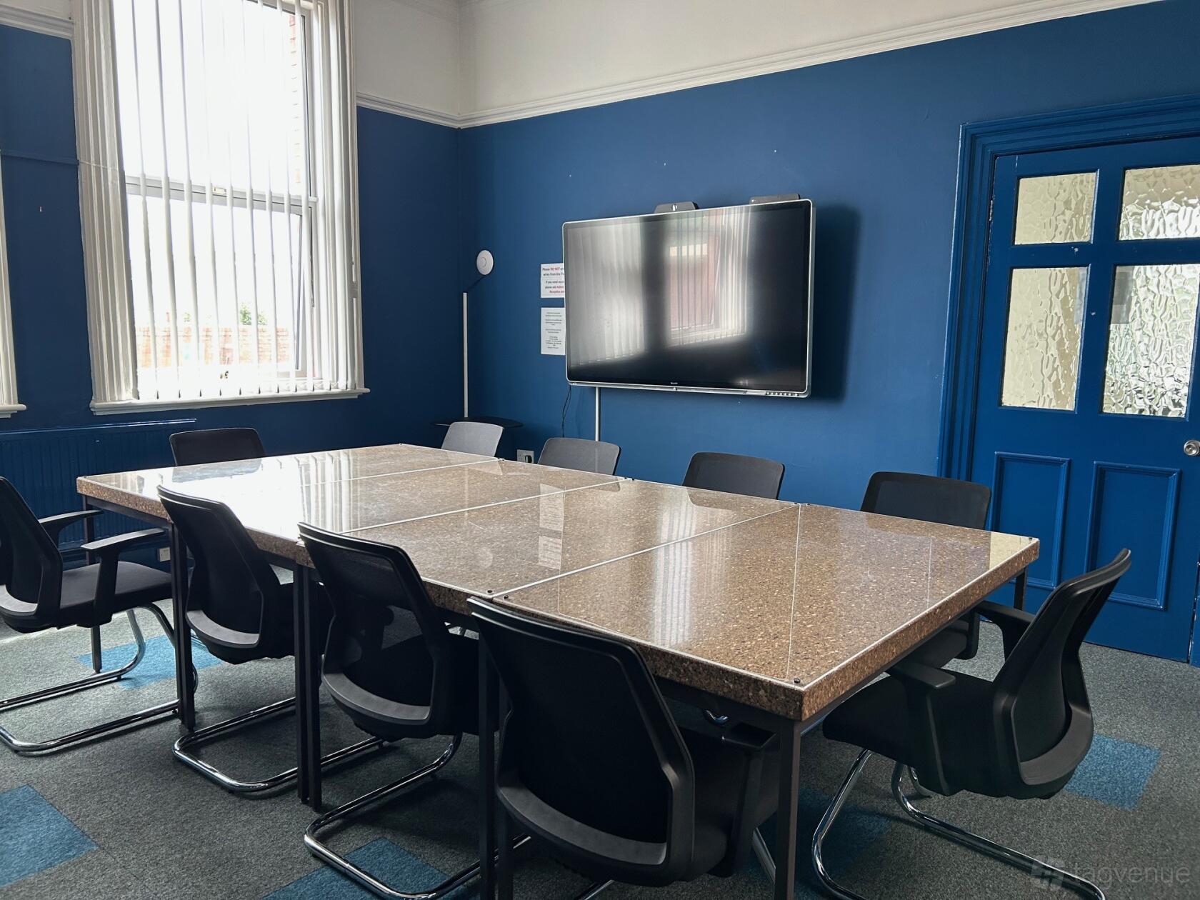 A meeting room with a large rectangular table, black chairs, and a wall-mounted screen at Voluntary Action Leeds - Stringer House.