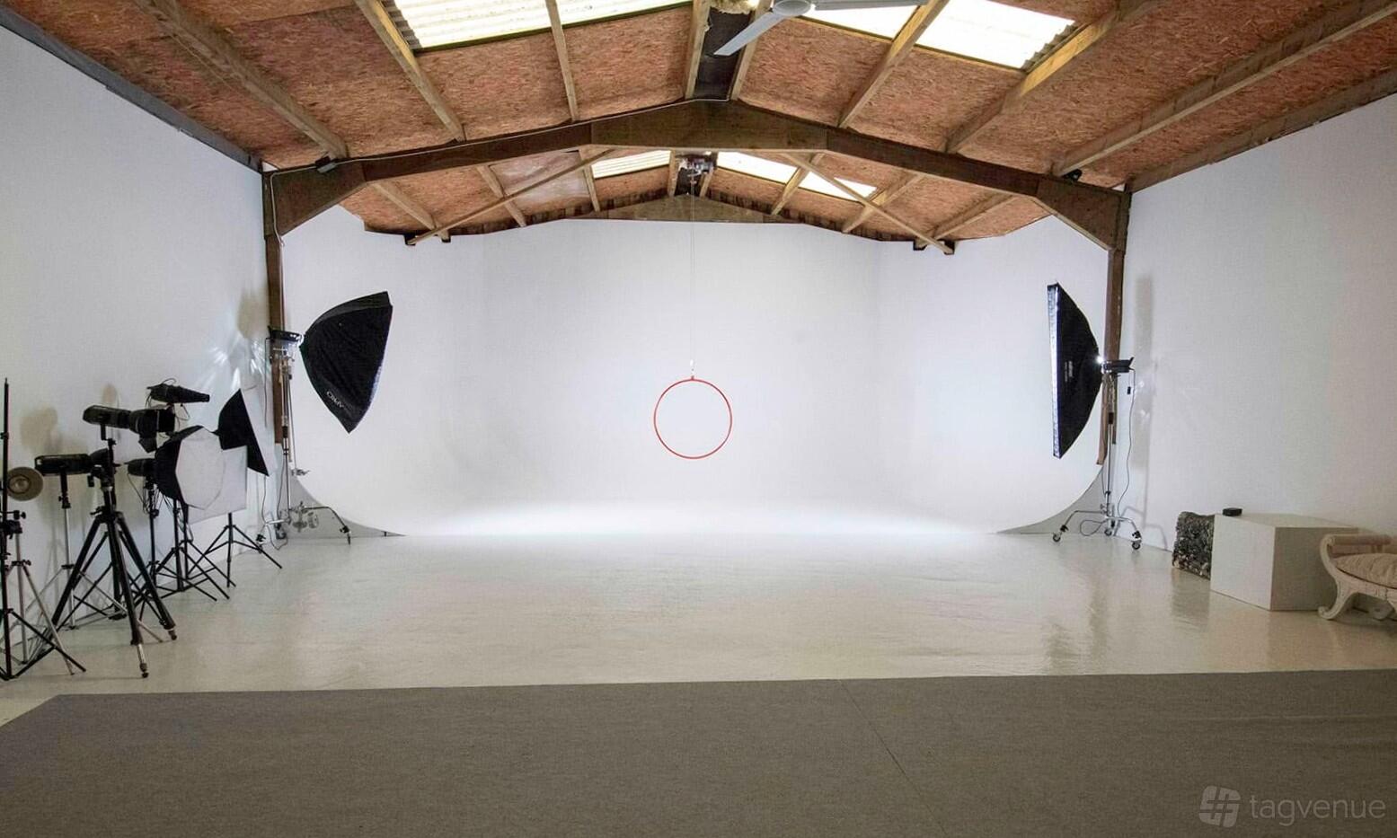 A photo studio with white cyclorama walls, exposed wooden ceiling beams, and professional lighting equipment at Somerset Studio.