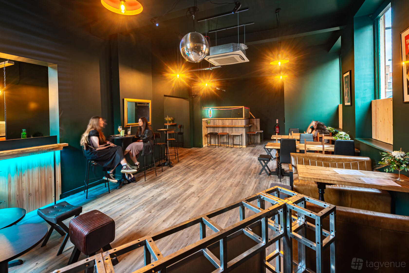 A cocktail bar with wood floors, teal walls, a disco ball, and neon lighting at The Loft Bar Leicester.