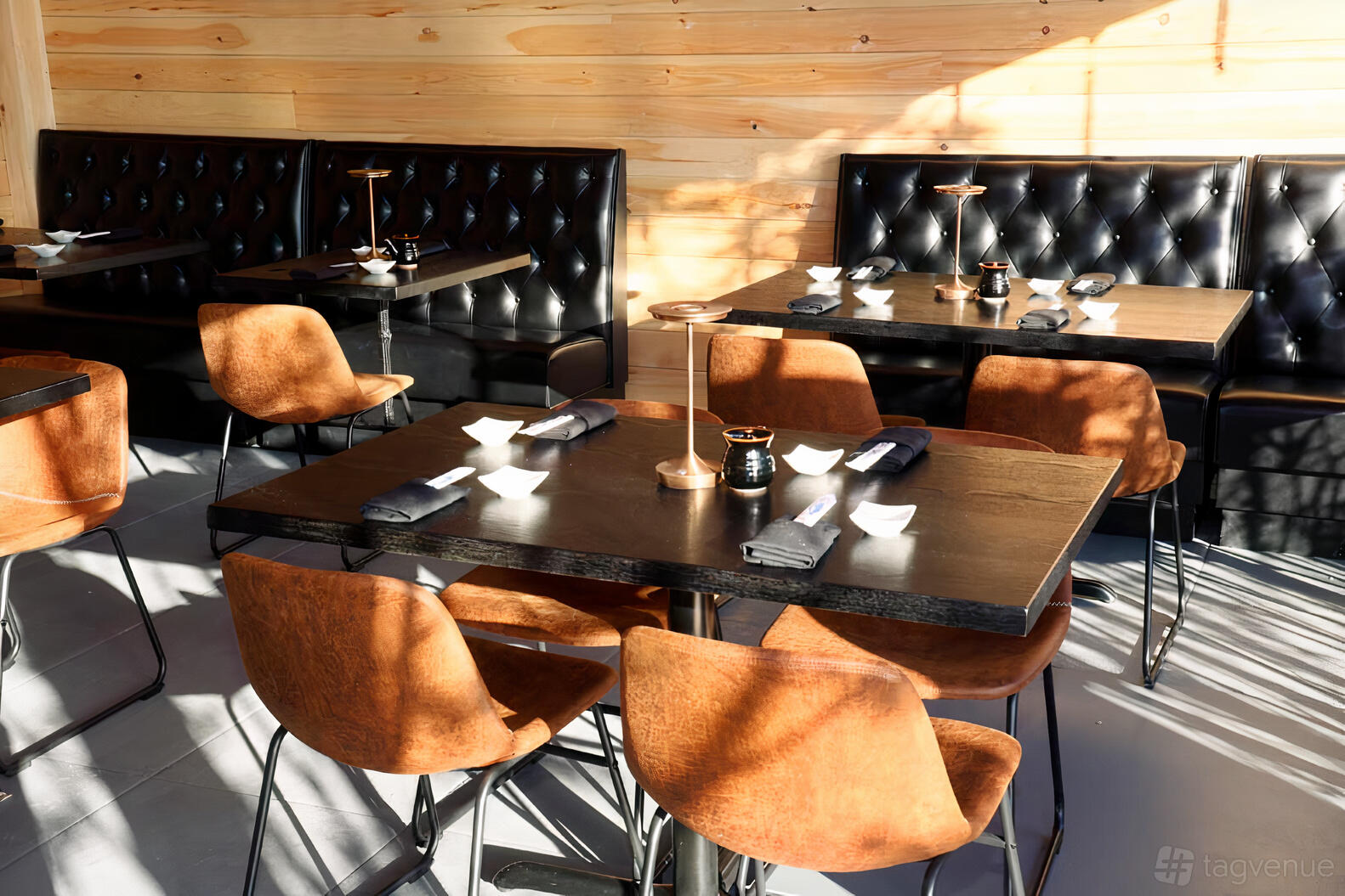 A restaurant with tan leather chairs, black tufted booths, wooden walls, and tables set for dining at Namiro Sushi.