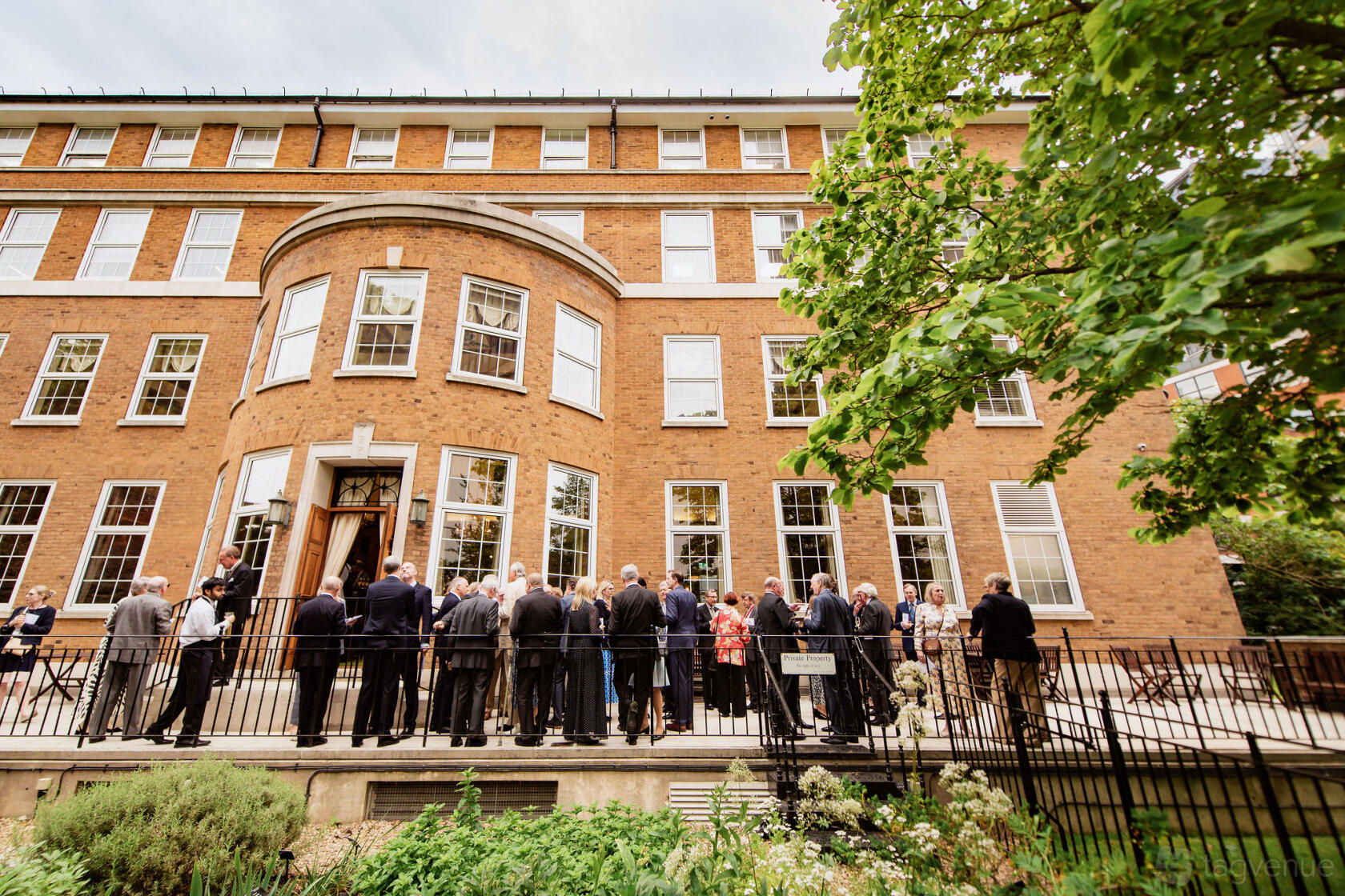 A terrace at a hall with people gathering, iron railings, and landscaped garden beds at Barber-Surgeons’ Hall.