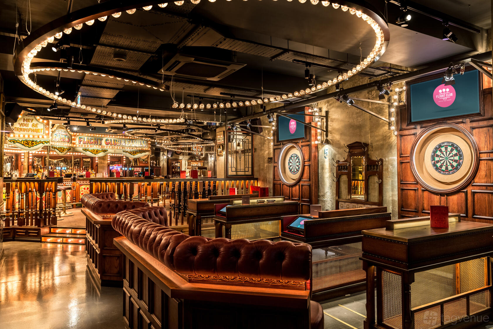 An event space in a bar with dartboards, leather banquettes, and circular overhead lighting at Flight Club Bloomsbury.
