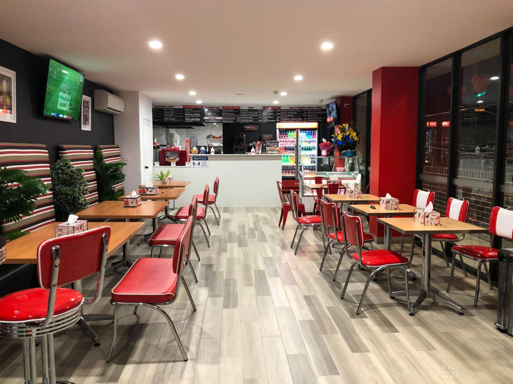 A dining room with red and white chairs, striped booth seating, and wood-look flooring at Uncle John Pizza.