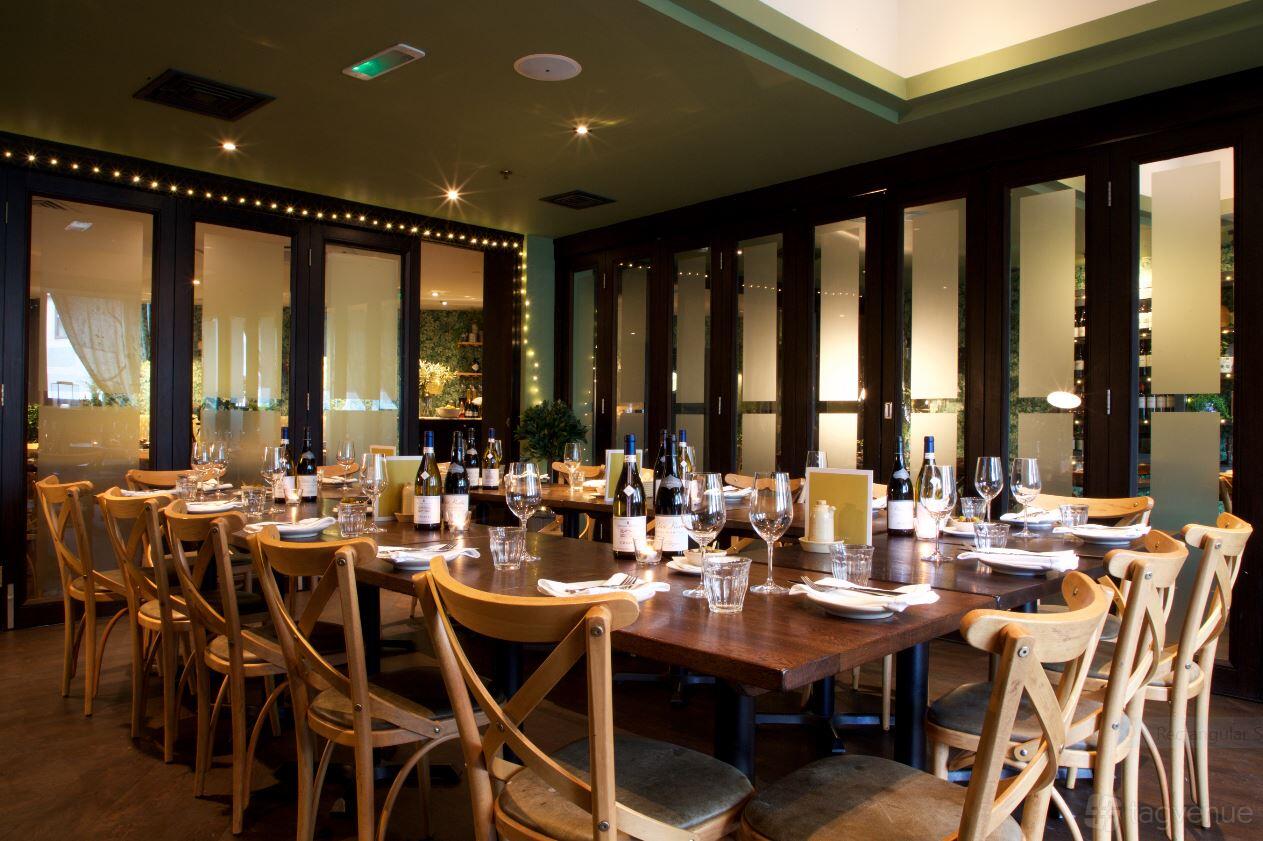 A dining room with a long wooden table set with wine bottles and glasses, surrounded by wooden chairs at Brasserie Blanc Southbank.