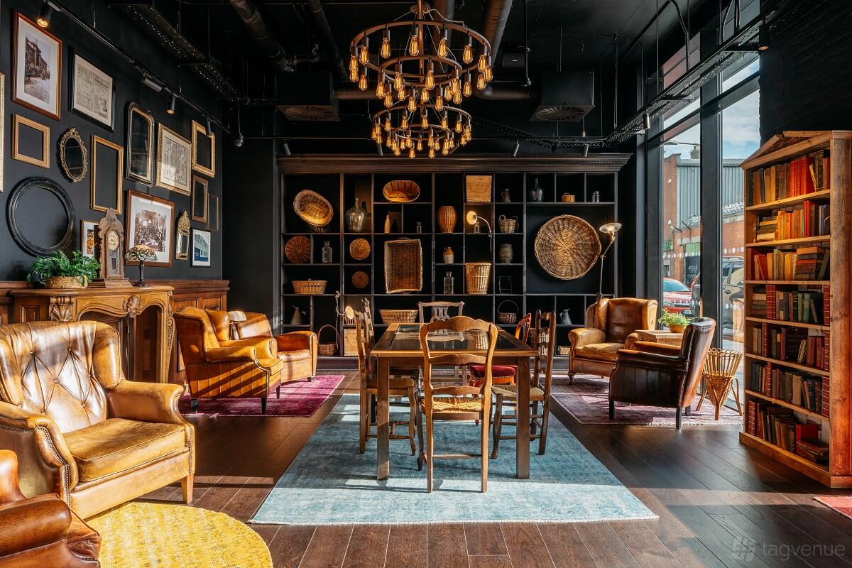 A hotel lounge with leather armchairs, bookshelves, chandeliers, and natural light at Ruby Molly Hotel & Bar.