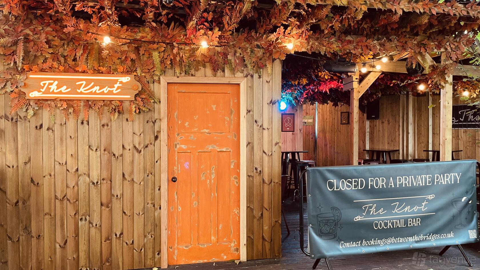 An event venue with wood paneling, orange door, and autumn leaf decorations at Between the Bridges.