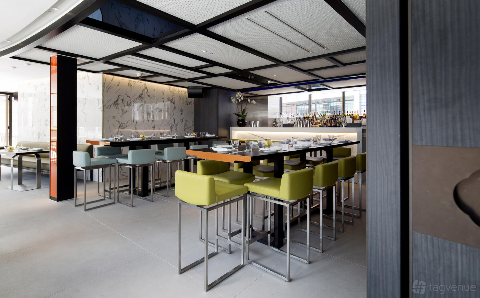 A restaurant dining room with marble wall accents, colorful bar stools, and a long communal table at Yauatcha City.