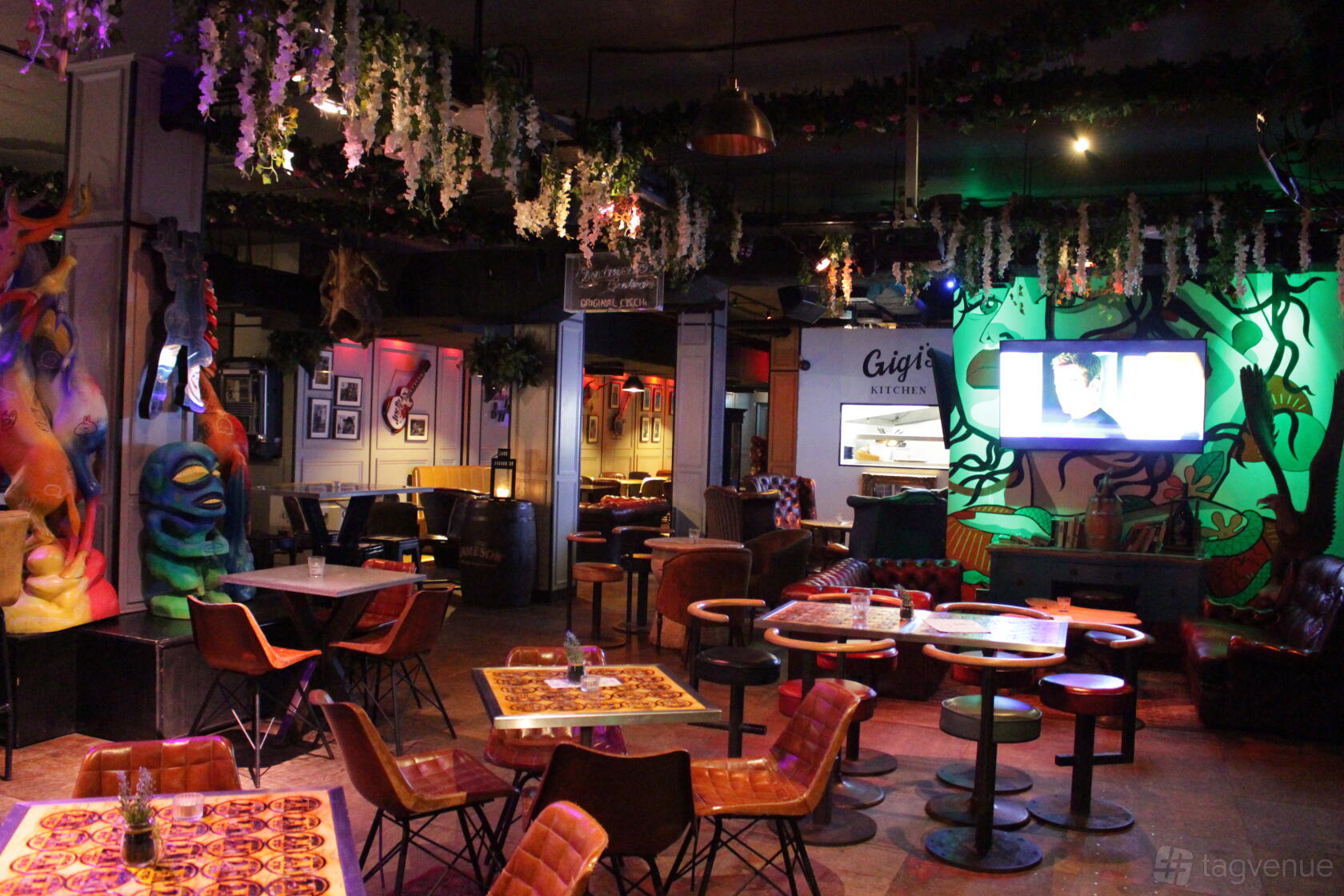 An event space with eclectic wall art, hanging greenery, and colorful seating at Gigi's Hoxton.