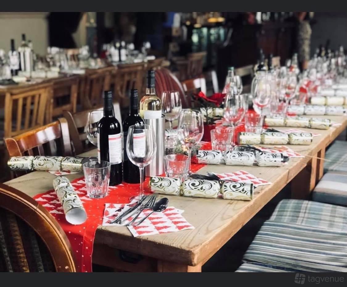 A function room in a pub with wooden tables set with wine bottles, glassware, crackers, and festive napkins at The Angelic.