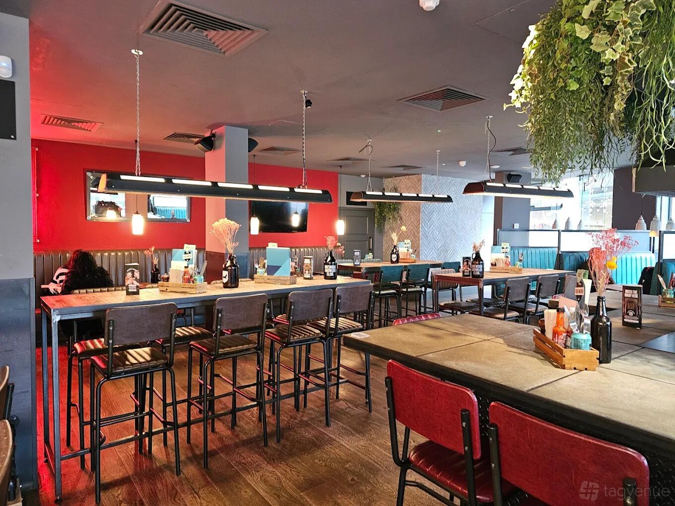 A lively bar with high tables, industrial lighting, and red accent walls at BrewDog Ealing.