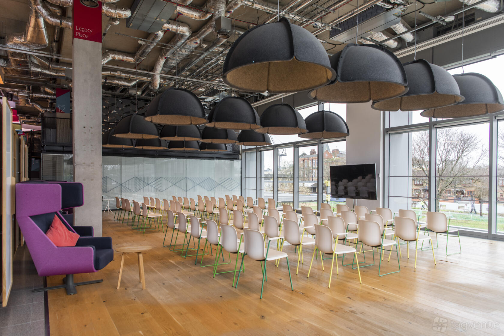An event space in a coworking venue with rows of white chairs, large black dome lights, and floor-to-ceiling windows at PLEXAL.