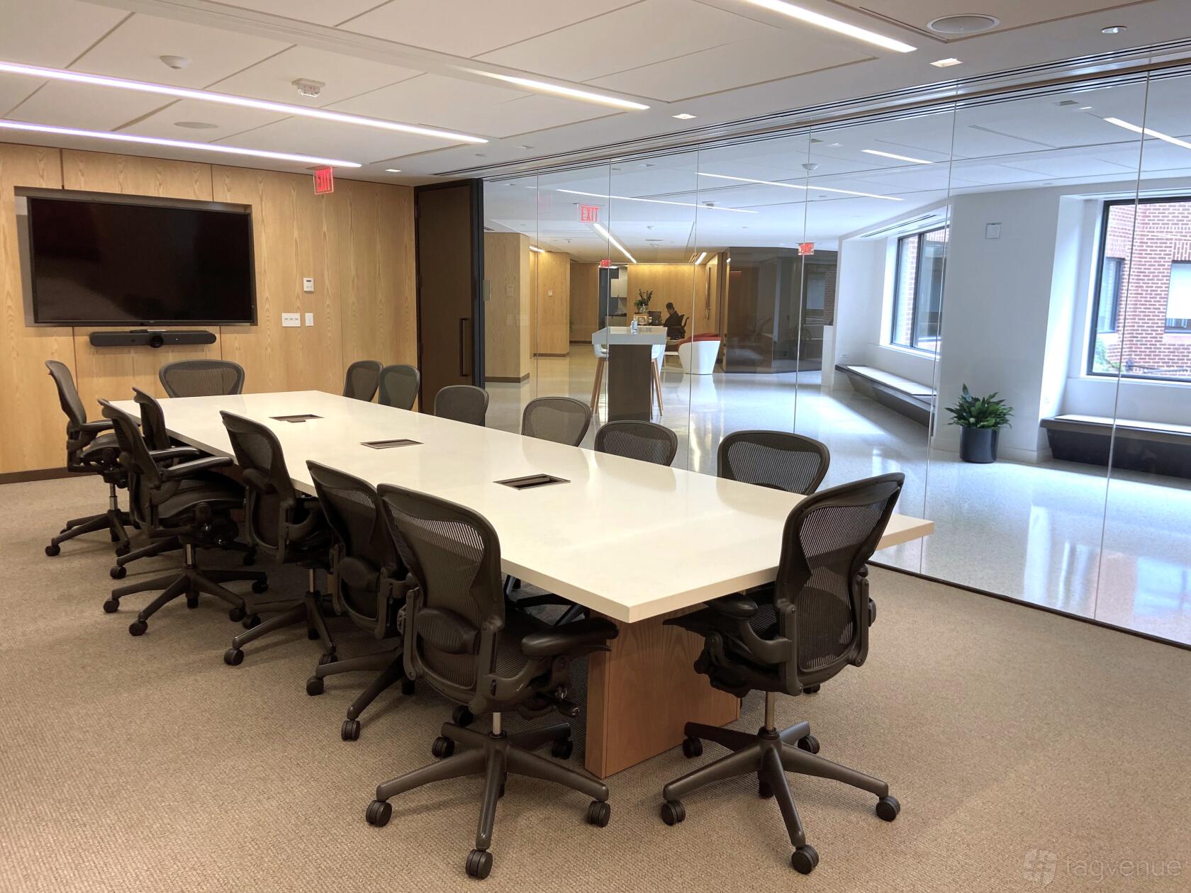 A boardroom with a long white table, ergonomic chairs, wall-mounted screen, and glass walls at AdvantEdge Workspaces.