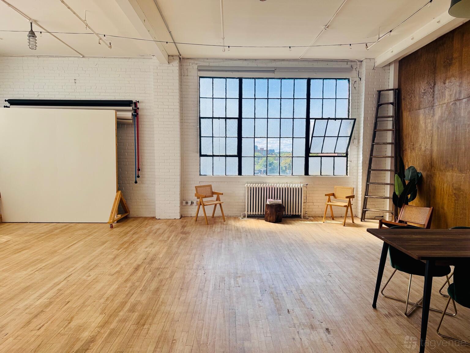 A loft with large industrial windows, white brick walls, wood floors, and studio chairs at Professional Photography Studio / Wade Studio.