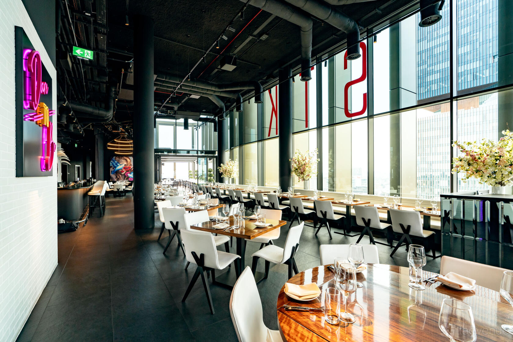A restaurant with floor-to-ceiling windows, neon signage, and set tables with glassware at STK Rooftop - Stratford.