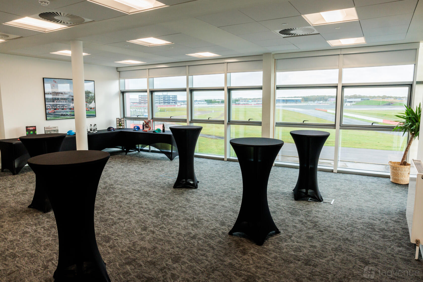 A meeting room with floor-to-ceiling windows, high-top tables, and views of the racetrack at Silverstone Museum.