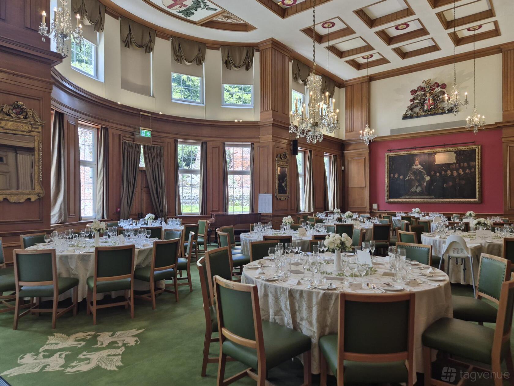 A grand hall with high windows, wood paneling, round tables set for dining, and chandeliers at Barber-Surgeons’ Hall.