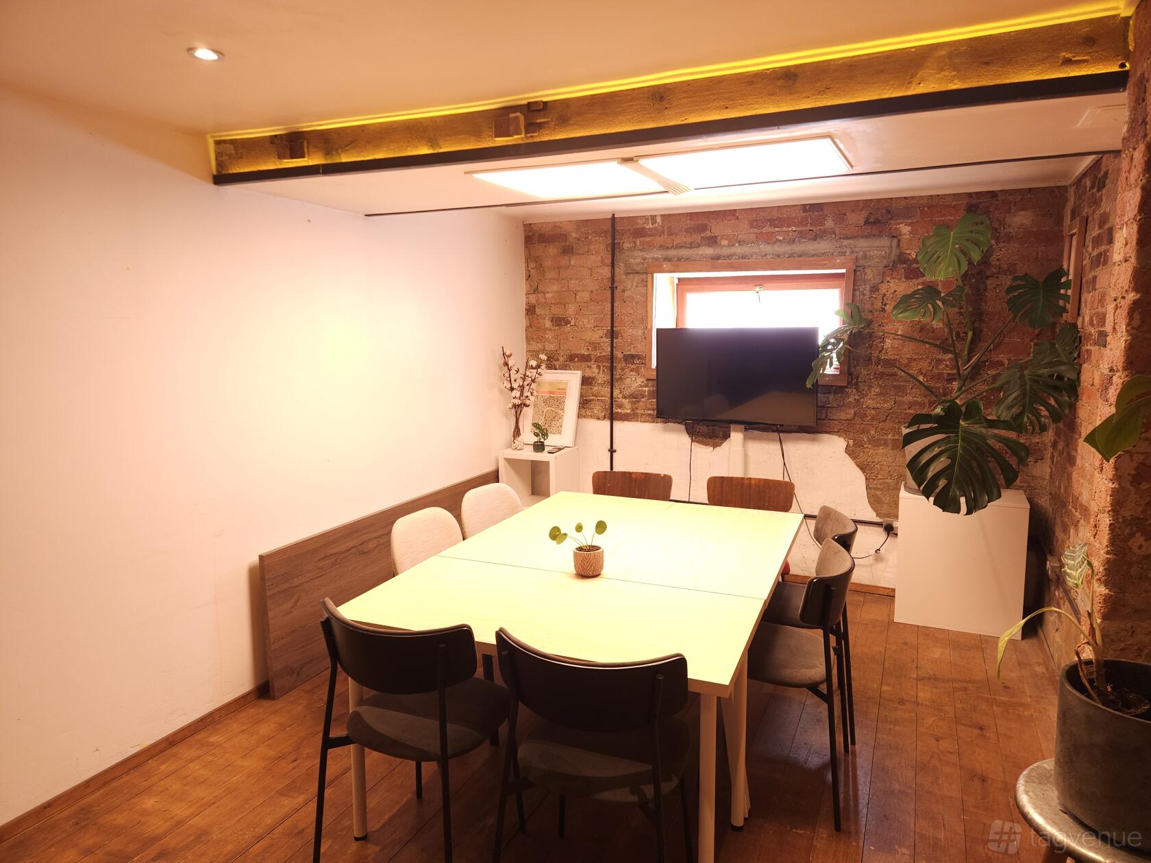 A meeting room with exposed brick walls, potted plants, and a central table with chairs at The Travel Cafe Holloway.