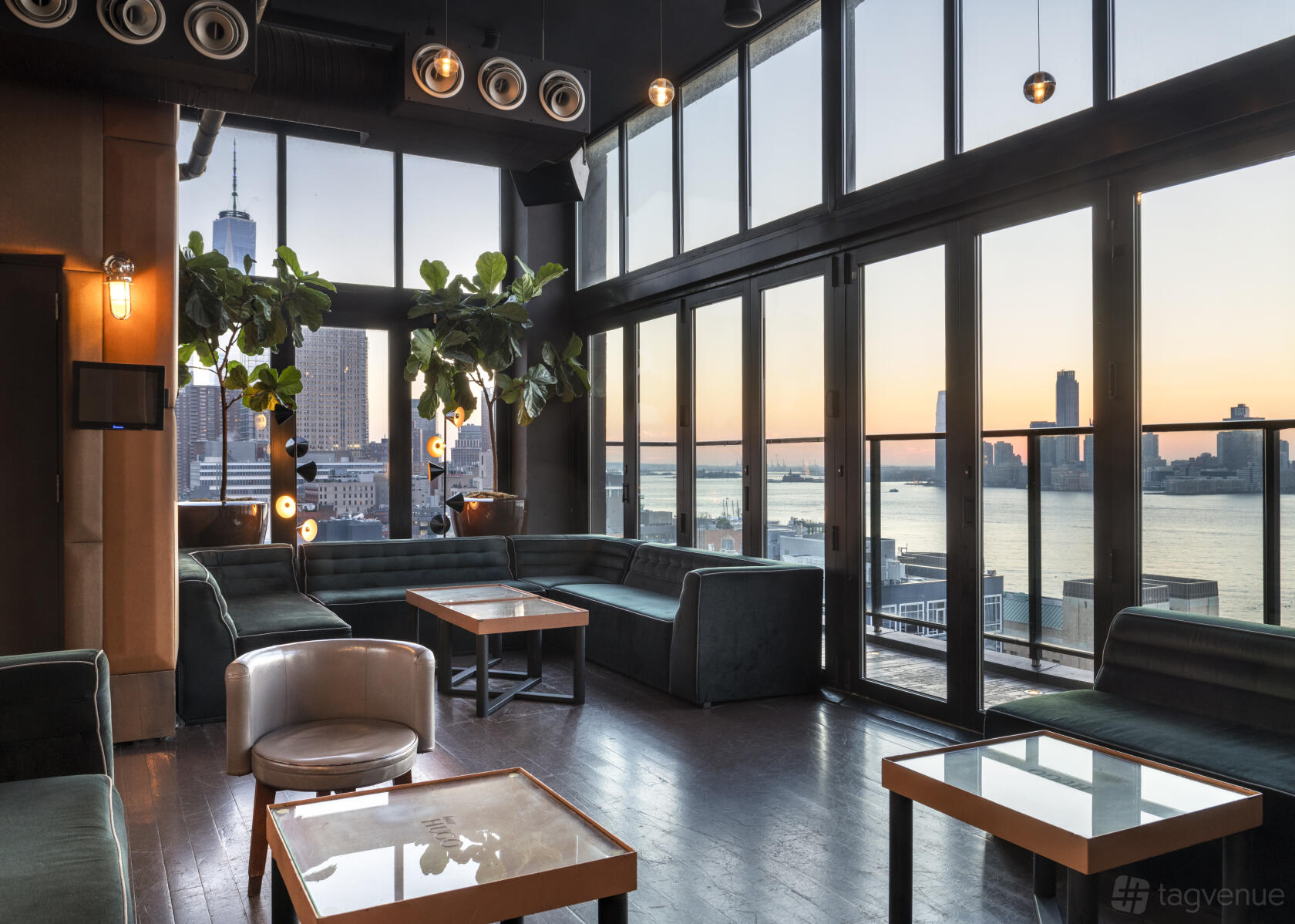 A hotel bar with floor-to-ceiling windows, navy velvet seating, and river views at Hotel Hugo SoHo.