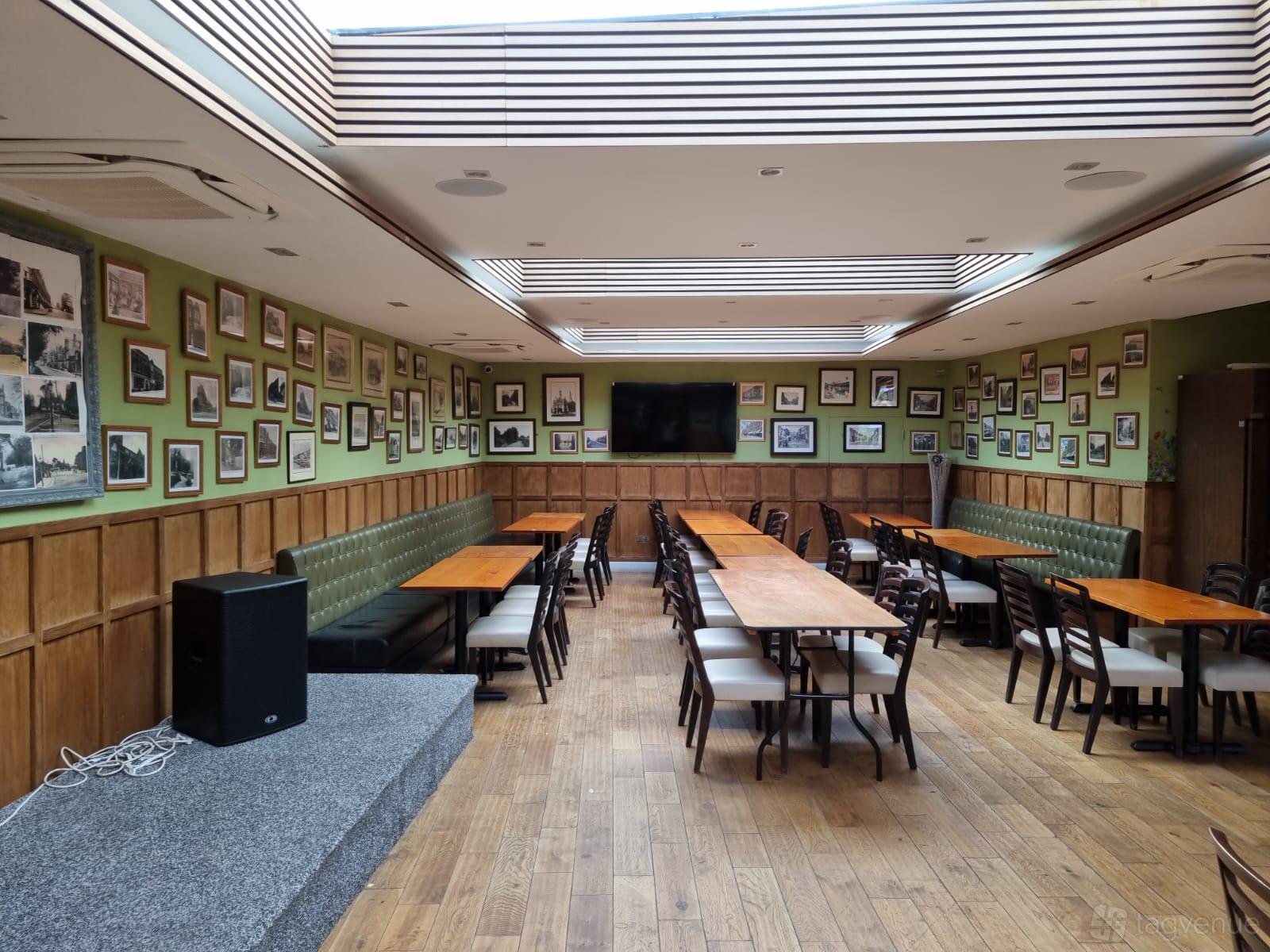 A pub terrace with skylights, wood flooring, banquet seating, and framed photos on green walls at Clissold Arms.