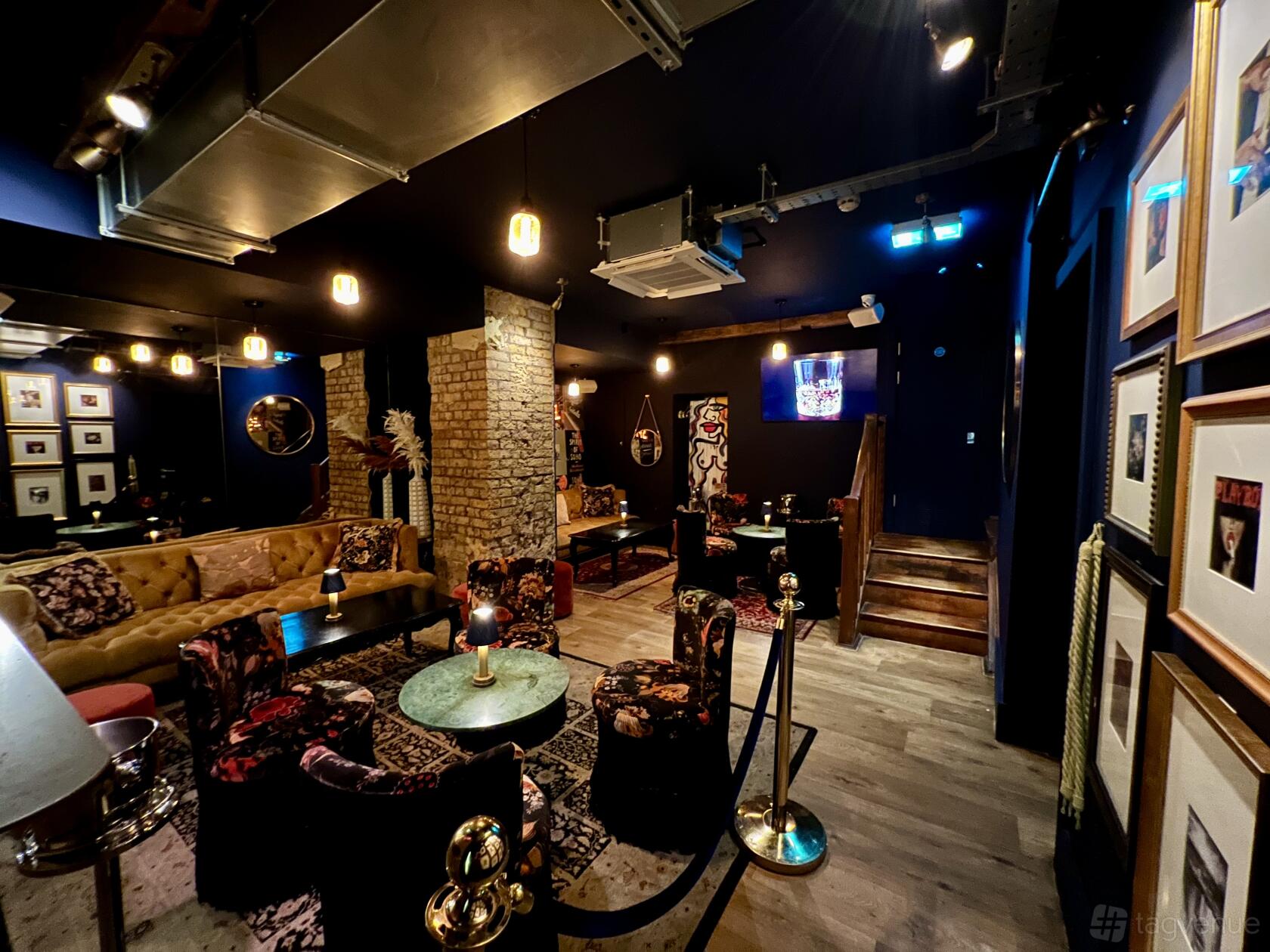 A lounge with exposed brick columns, velvet seating, eclectic decor, and framed art at Baaria.