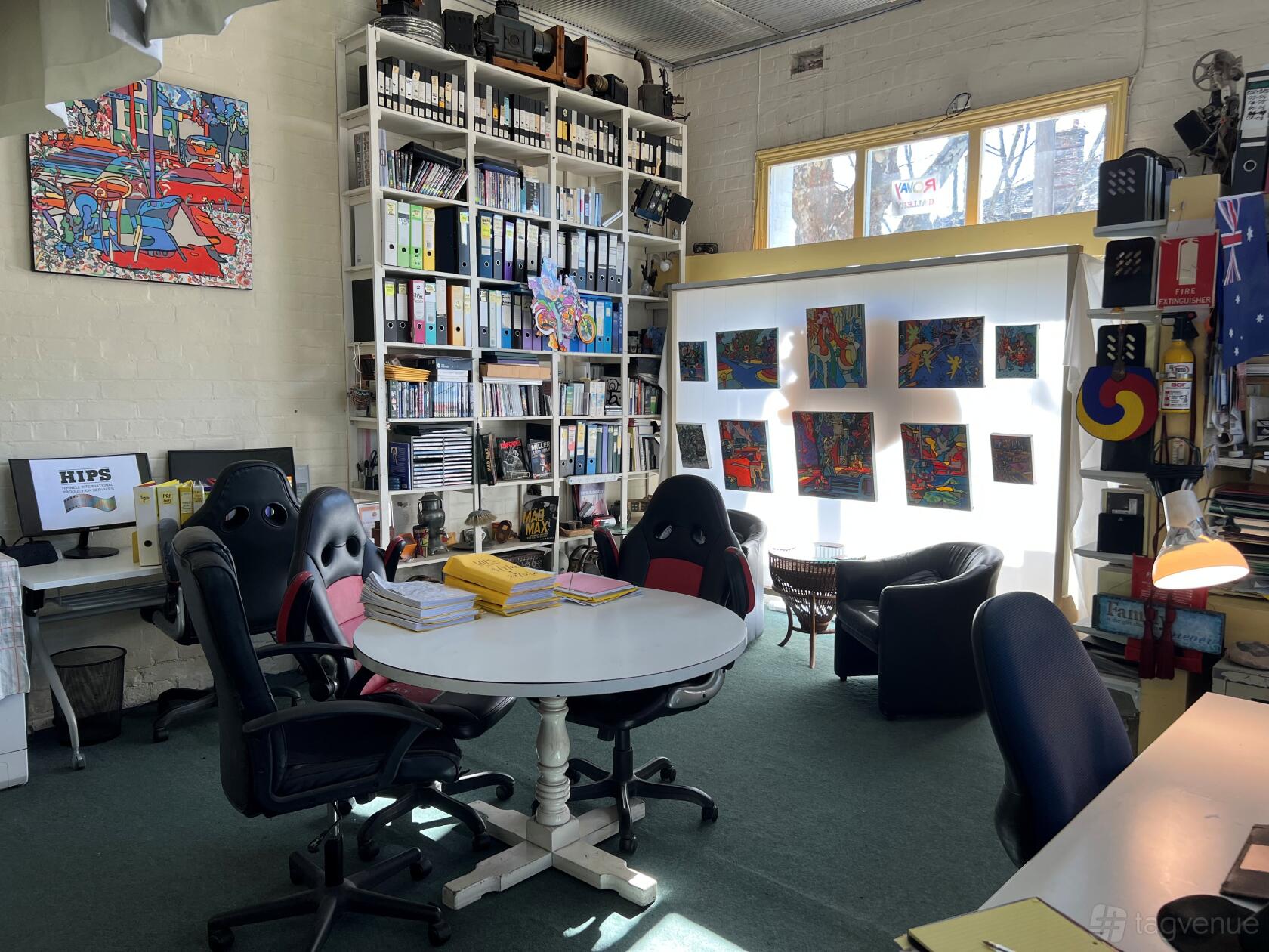 A film studio office with tall bookshelves, colorful artwork, and round meeting table at Hipwell International Production Services.