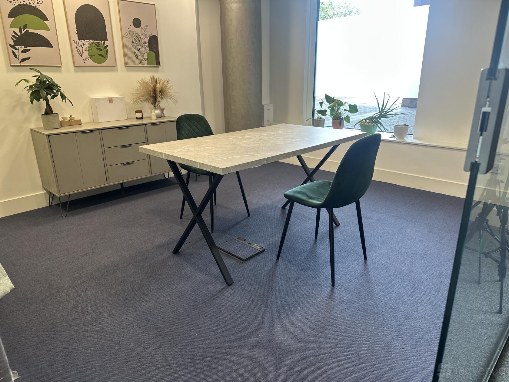 A creative space with a marble-top table, green chairs, wall art, and potted plants near large windows at Elty Life Store.