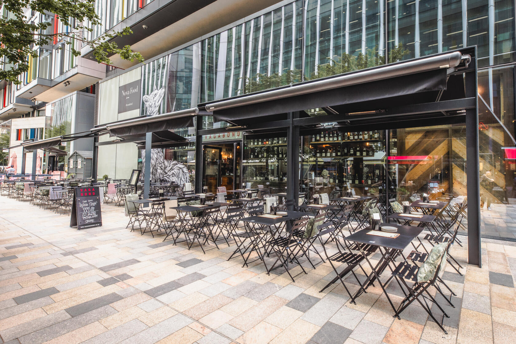An outdoor lounge with black metal tables and chairs under retractable awnings at Vagabond Victoria.