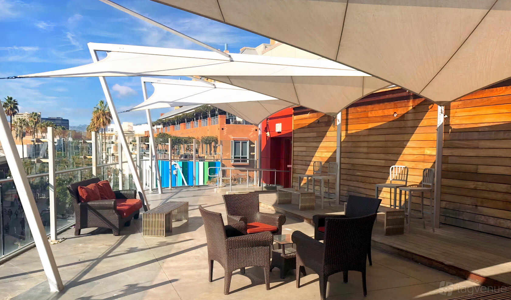 An outdoor event venue with wicker lounge seating, wood-paneled walls, and large white shade sails at Dojo Events.