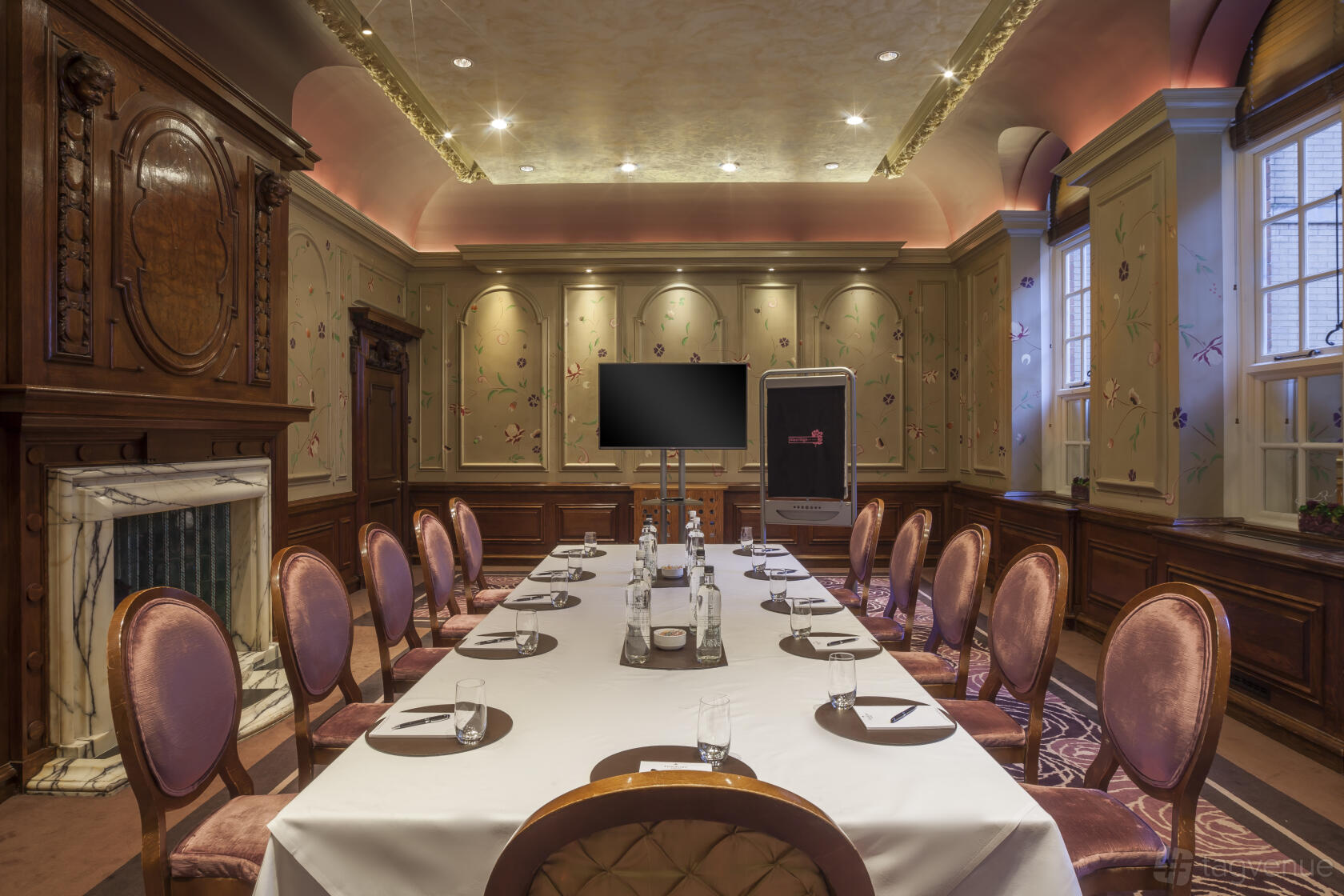 A hotel event room with ornate wood paneling, a marble fireplace, and a long boardroom table at The Roseate Reading.