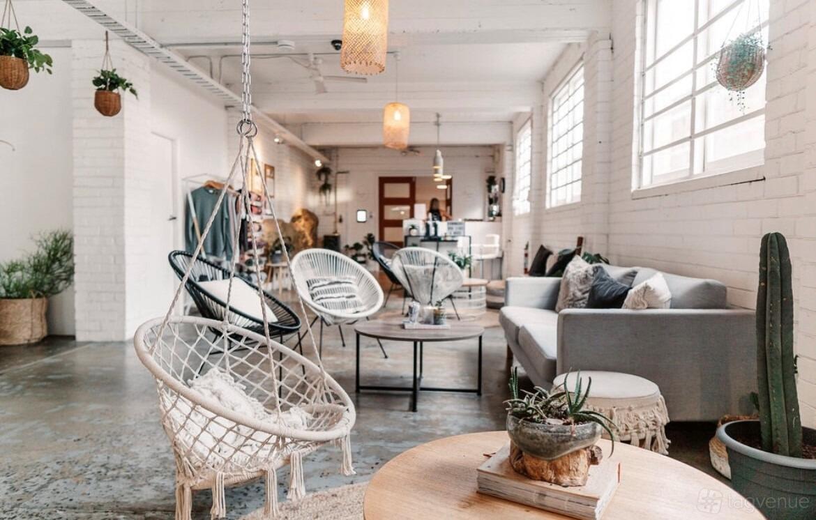 A yoga studio lounge with hanging chairs, sofas, potted plants, and natural light at Luxe Yoga & Fitness.