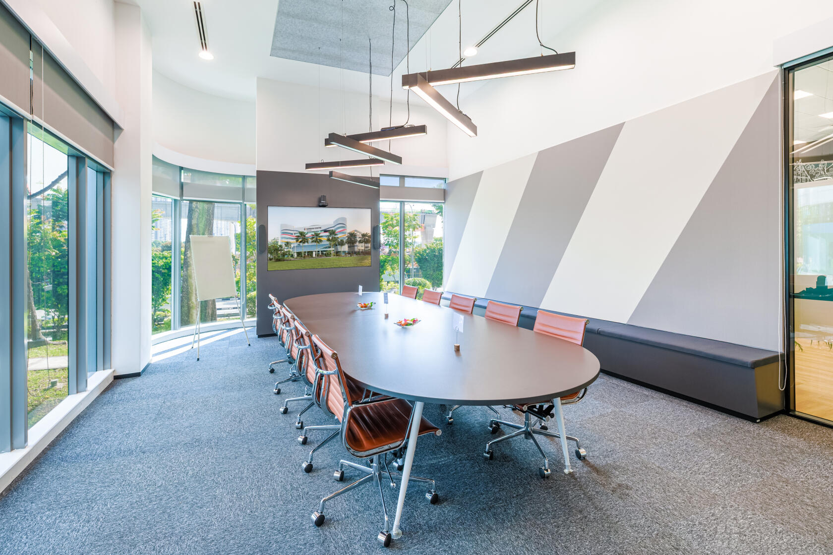 A boardroom with a long oval table, modern chairs, large windows, and geometric wall panels at German Centre Singapore.