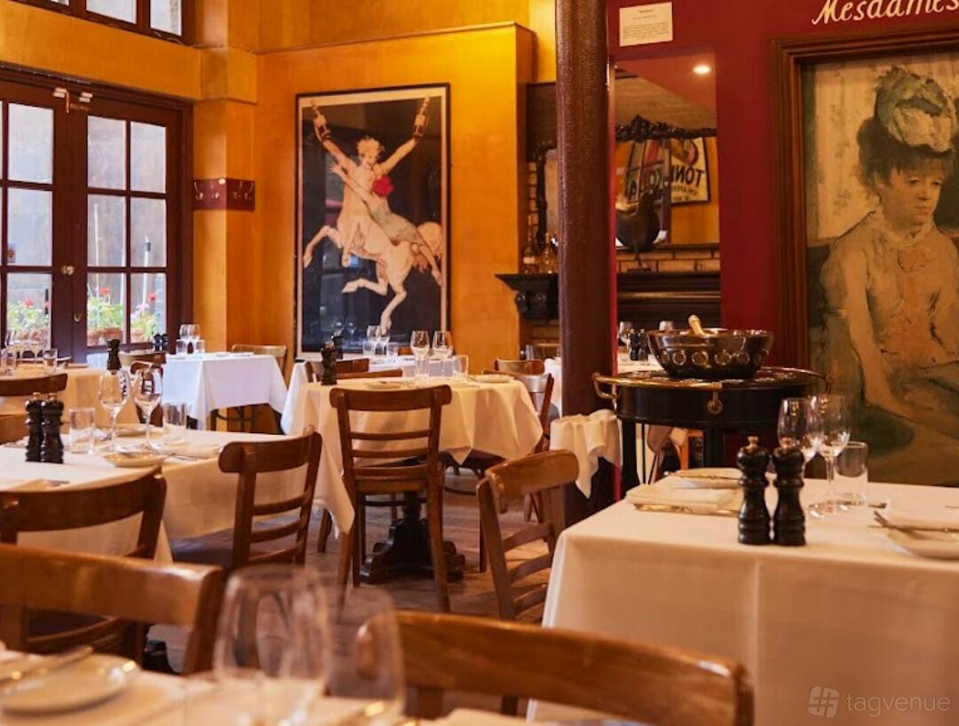 A restaurant dining room with wooden chairs, white tablecloths, and vintage artwork at Bleeding Heart.