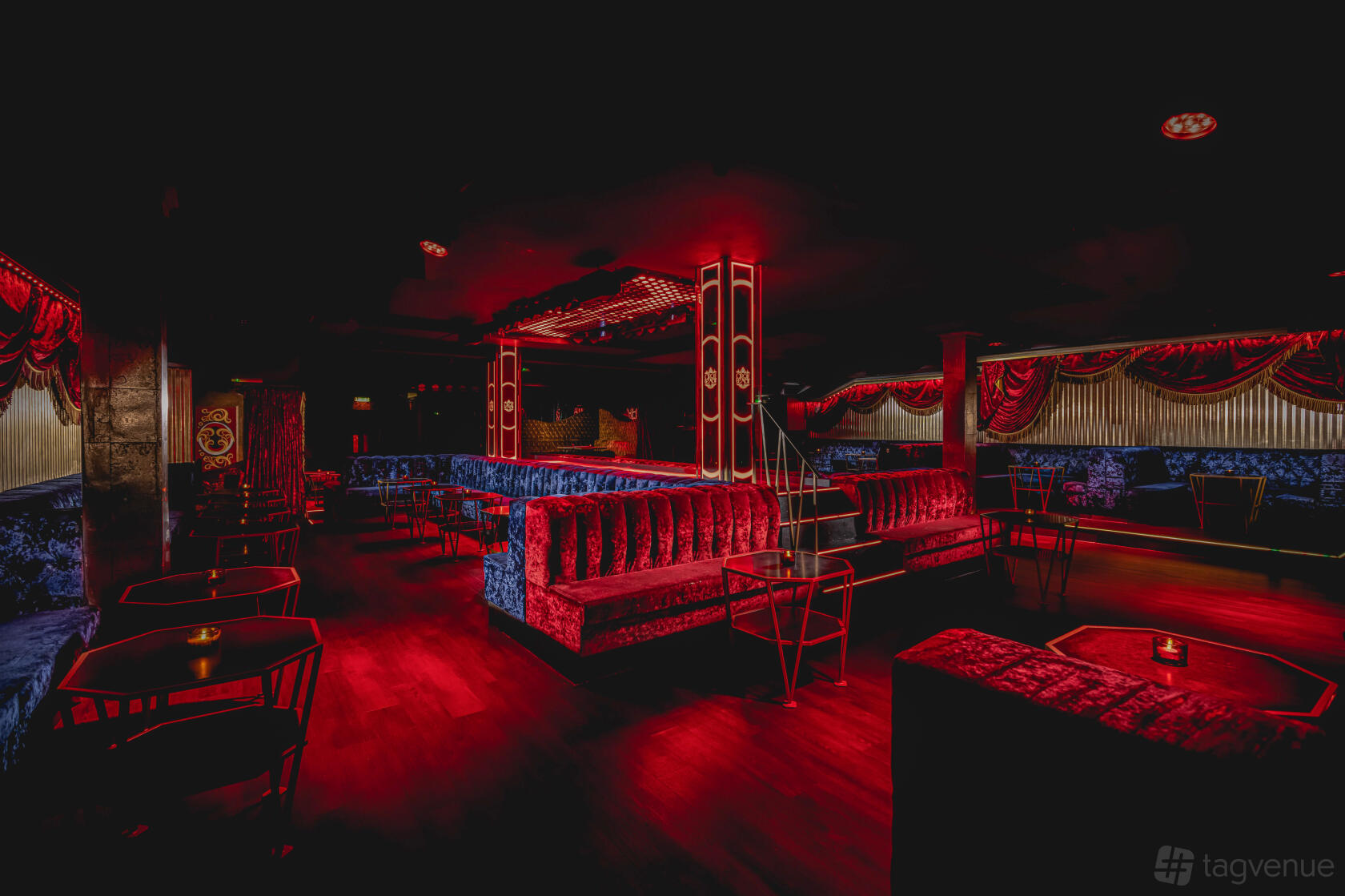 A nightclub with plush red velvet booths, low lighting, and gold drapery at Cirque le Soir.