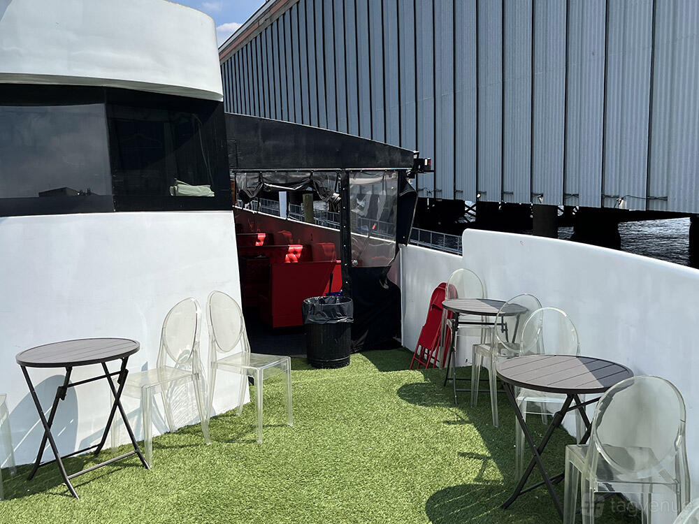 A yacht outdoor deck with artificial grass flooring, round tables, and clear chairs at Avalon Yacht – Skyport Marina NYC.