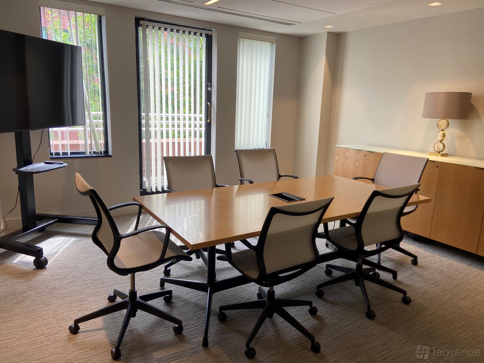 A boardroom with a wooden conference table, six swivel chairs, floor-to-ceiling windows, and a large screen at AdvantEdge Workspaces.