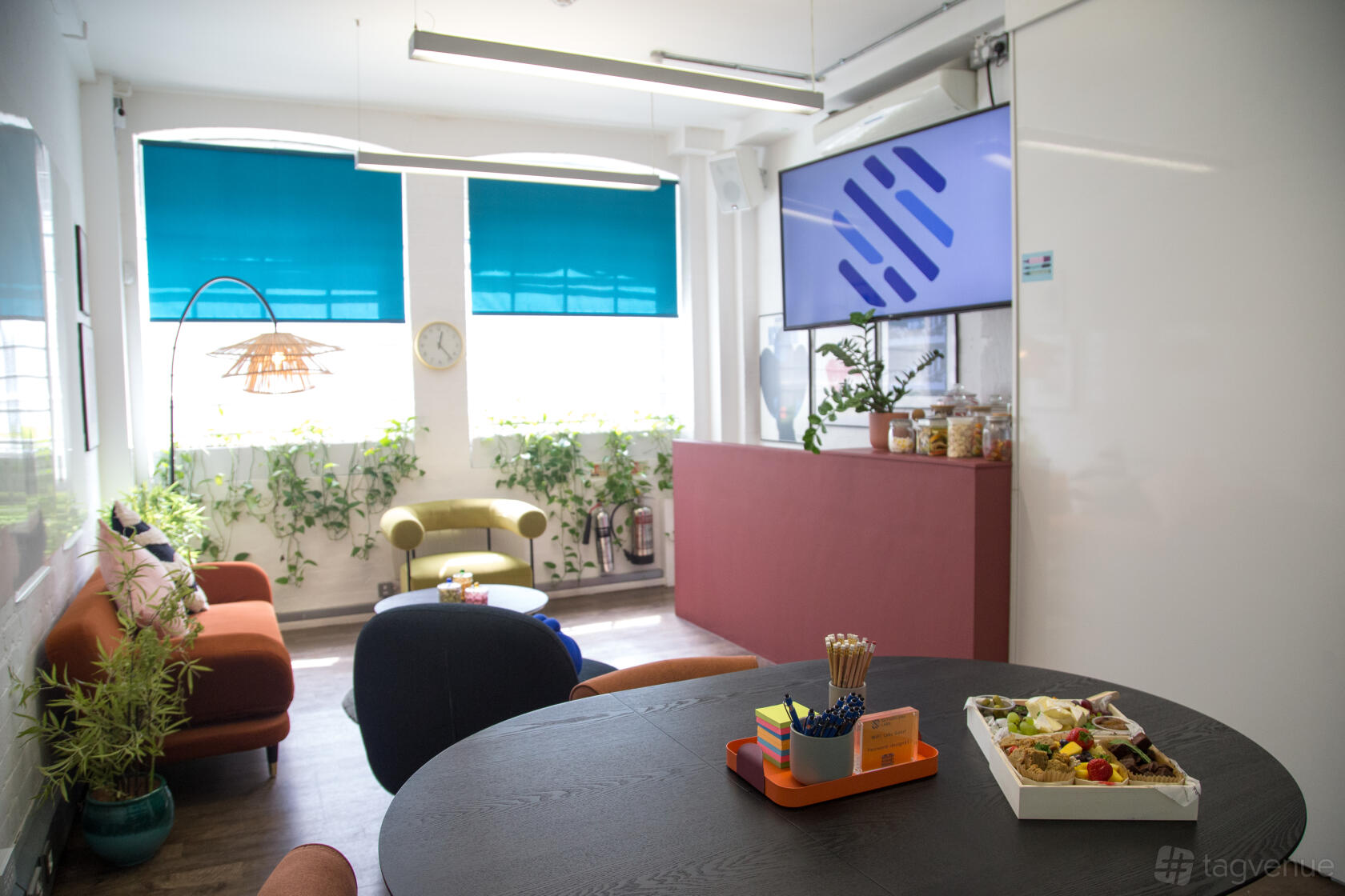 A meeting room with a round table, bright blue window shades, plants, and snacks at Sutherland Labs.